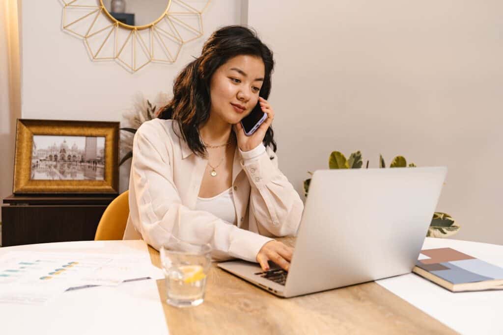woman on smart phone working on a laptop at her desk
